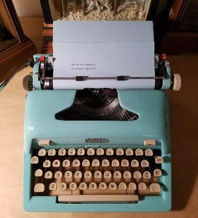 Vintage turquoise typewriter with white keys on a wooden table.